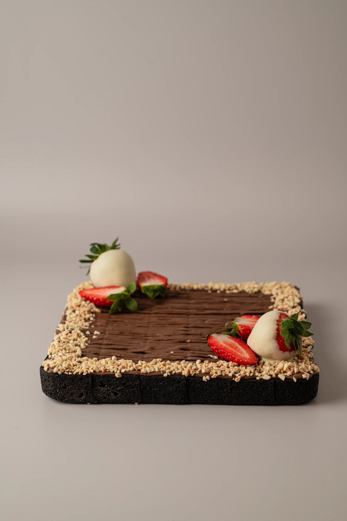 Brownie decorado sin gluten, sin azúcar y sin lactosa con nutelina, fresas frescas y almendras crujientes.
