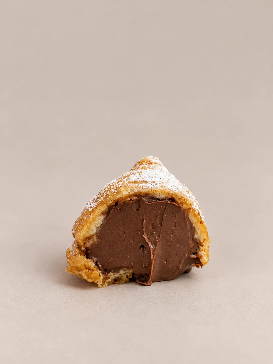 Buñuelo de chocolate sin gluten y sin lactosa con forma redondeada, relleno de chocolate y cubierto con azúcar glas.