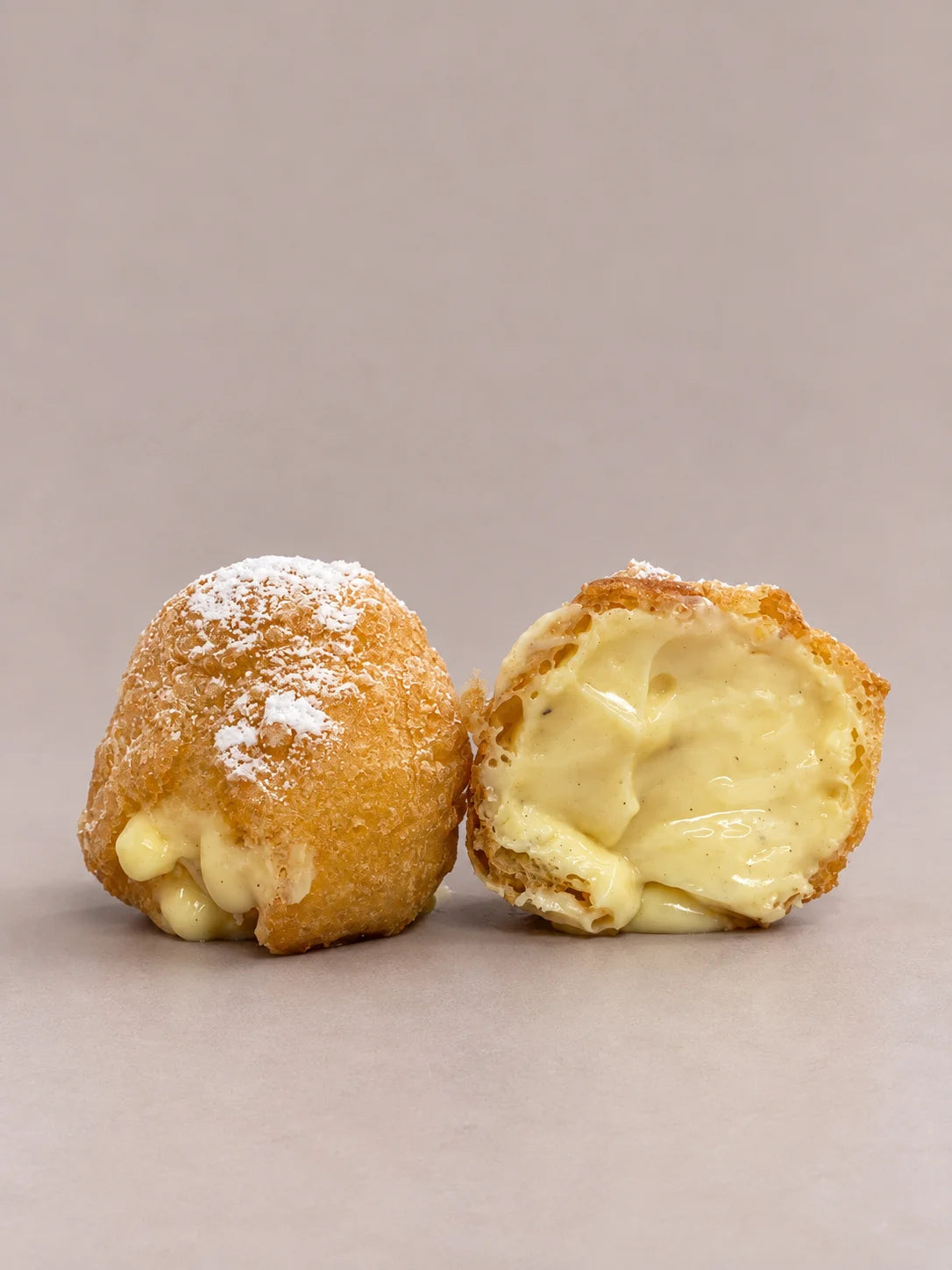 Buñuelo de crema sin gluten abierto junto a otro entero, con su relleno de crema suave y sedosa.