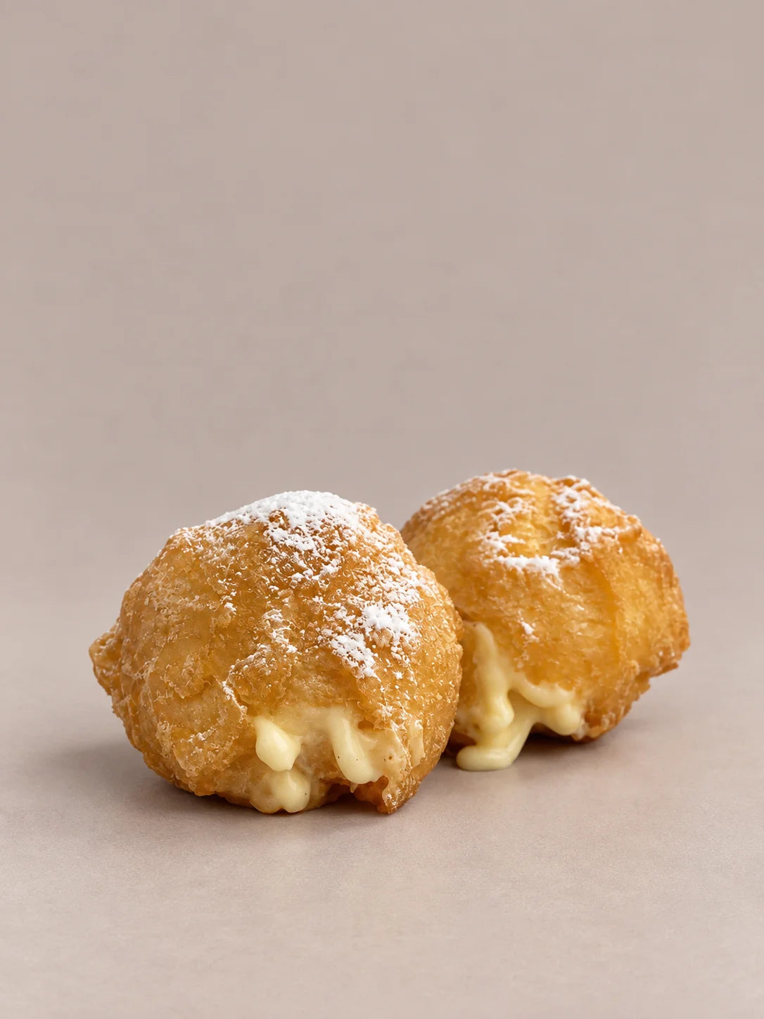 Buñuelos de crema sin gluten de NICOLINA Madrid, dorados, espolvoreados con azúcar y con la crema asomando.