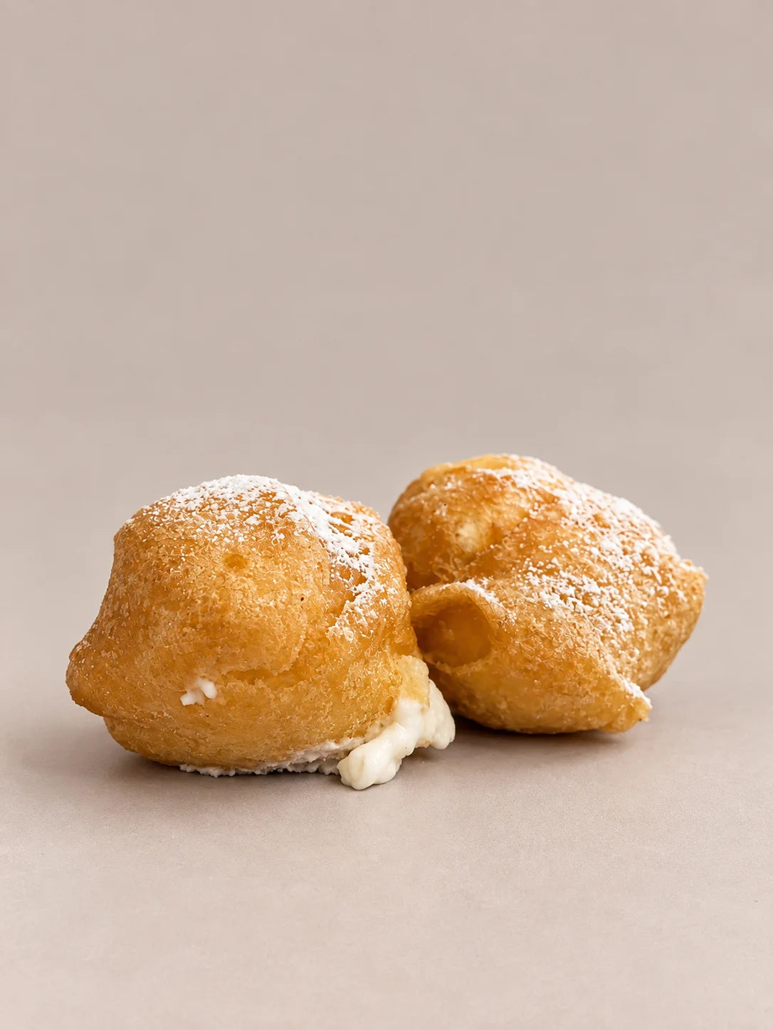 Buñuelos de nata sin gluten de NICOLINA Madrid, dorados, espolvoreados con azúcar y con la nata asomando.