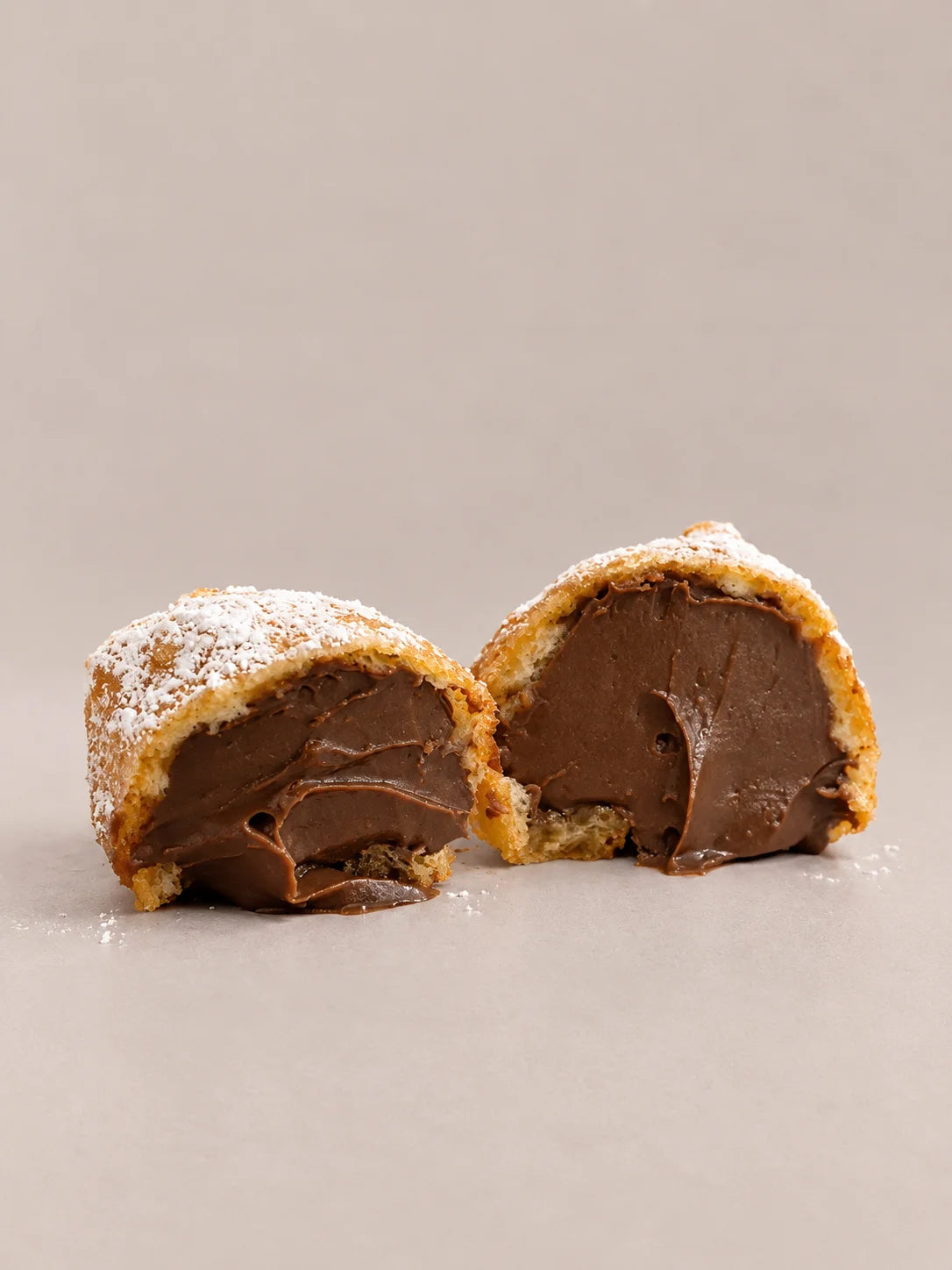 Dos buñuelos de chocolate sin gluten y sin lactosa, cortados y rellenos de chocolate cremoso, espolvoreados con azúcar.