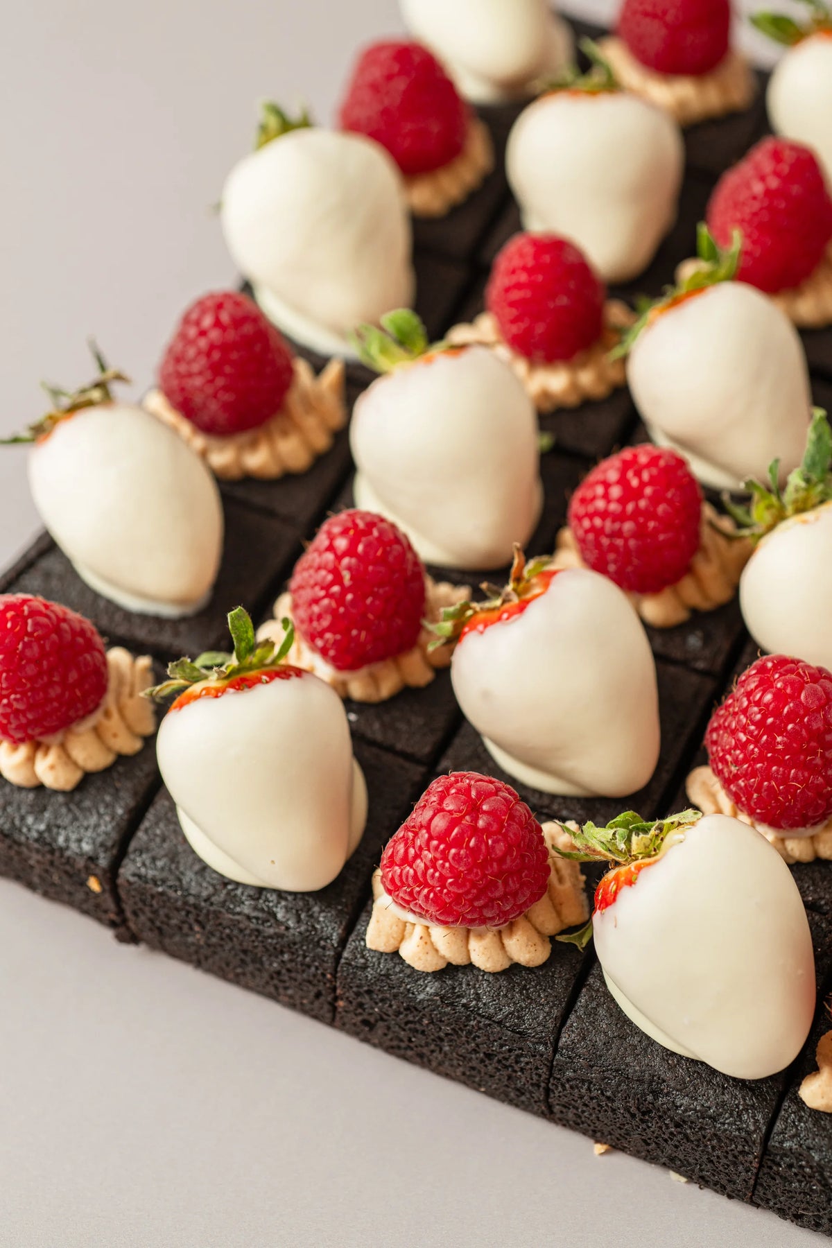 Detalle de brownies artesanales sin gluten, sin azúcar y sin lactosa con fresas bañadas en chocolate blanco y frambuesas.

