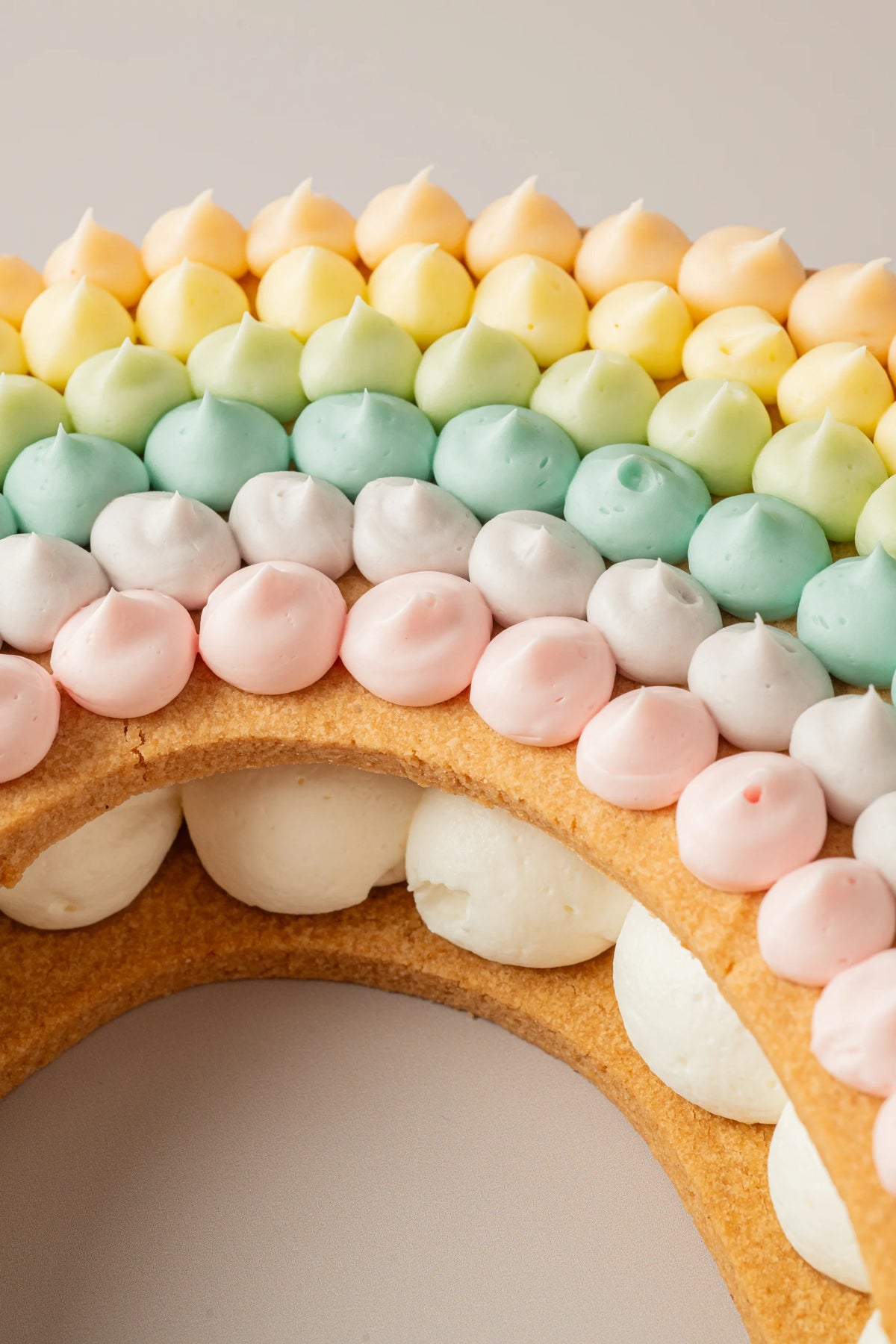 Detalle de tarta arcoíris sin gluten, sin azúcar y sin lactosa decorada con crema de colores pastel.

