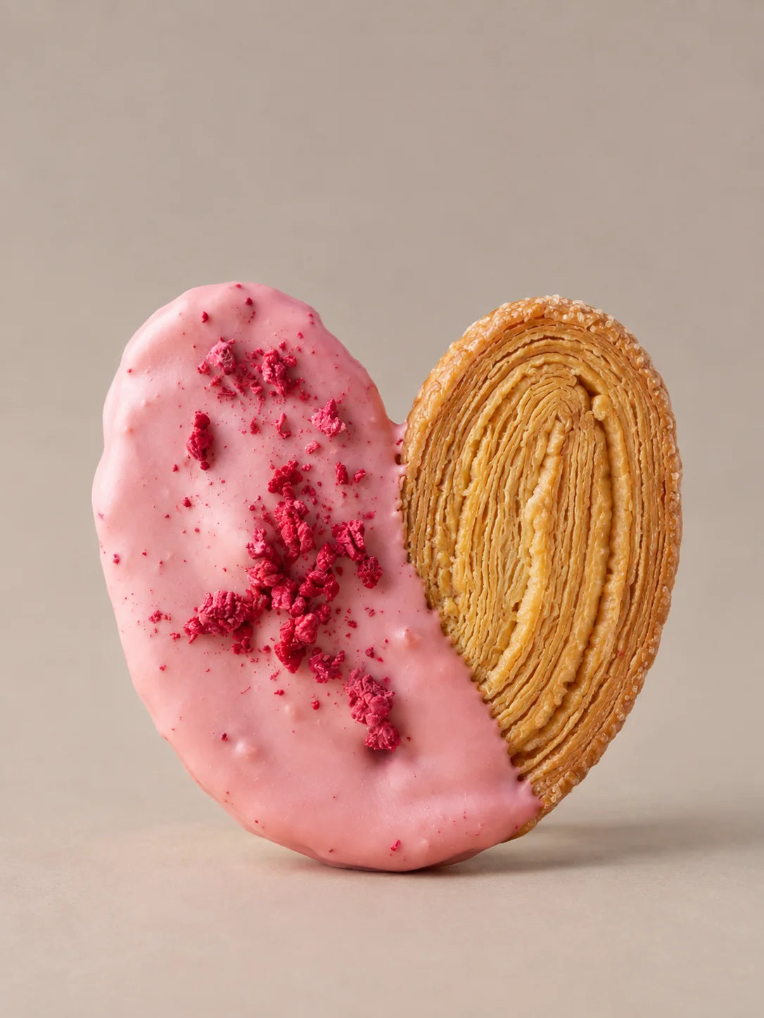 Palmera de frambuesa sin gluten con hojaldre crujiente, chocolate blanco rosa y trozos de frambuesa liofilizada.
