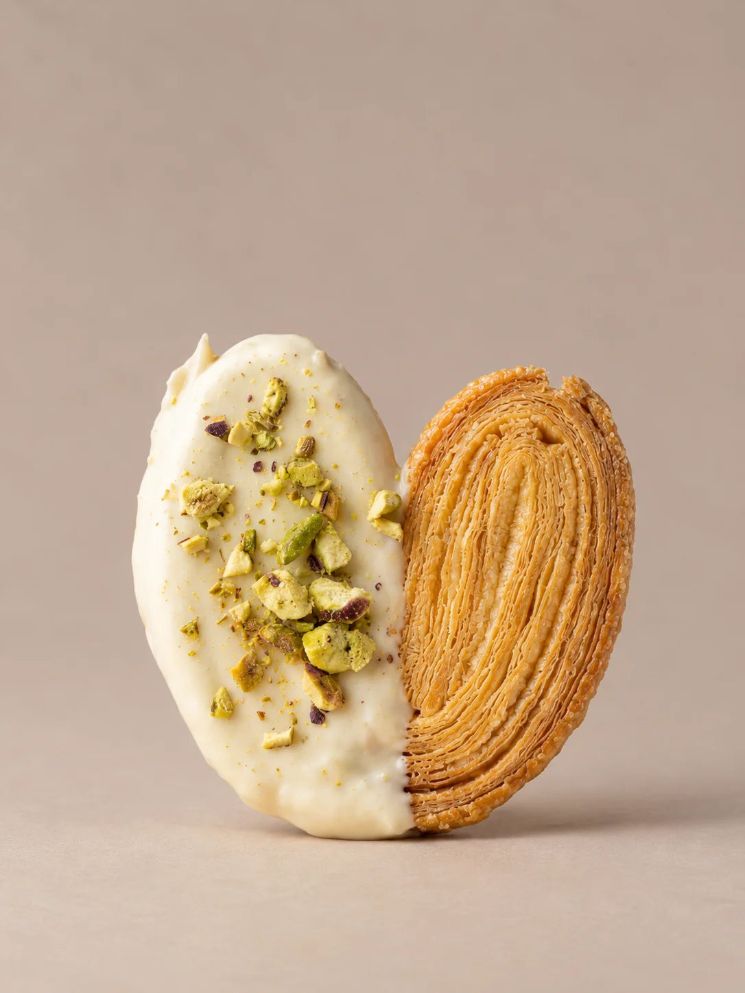 Palmera de pistacho sin gluten con hojaldre crujiente, cobertura de chocolate blanco y pistacho troceado.
