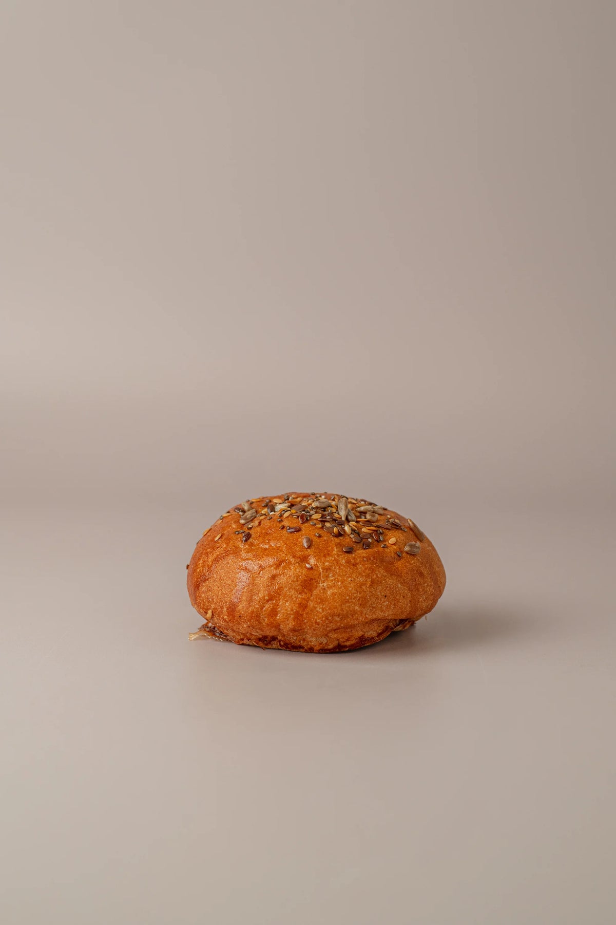 Pan de hamburguesa individual sin gluten, sin lactosa y sin azúcar con superficie dorada y semillas variadas.
