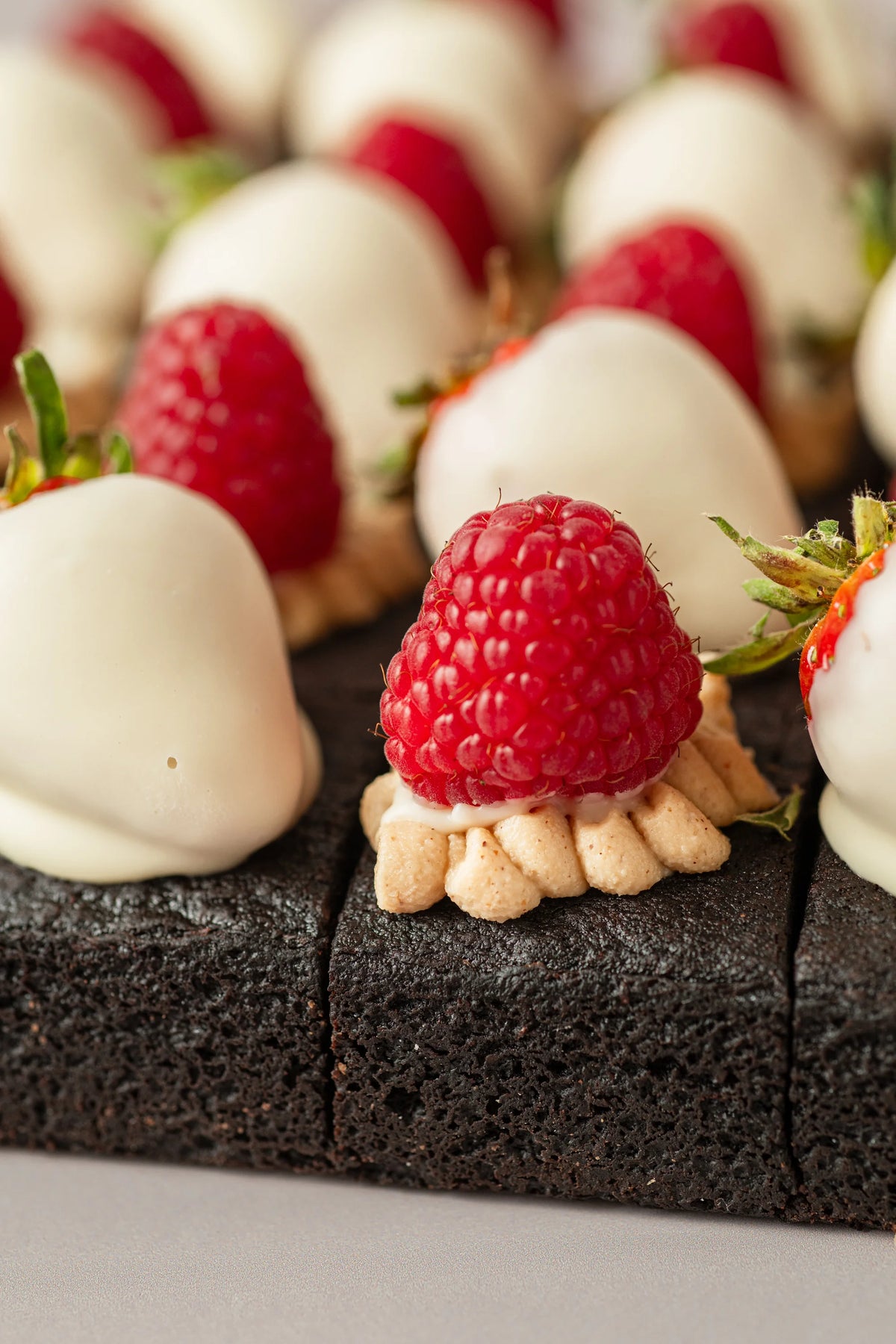 Primer plano de brownies sin gluten, sin azúcar y sin lactosa decorados con crema kinder, frambuesas y fresas bañadas.
