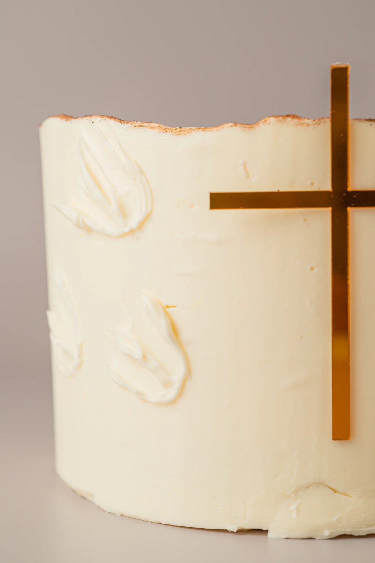 Detalle de tarta de comunión sin gluten con cobertura cremosa blanca y decoración minimalista dorada.
