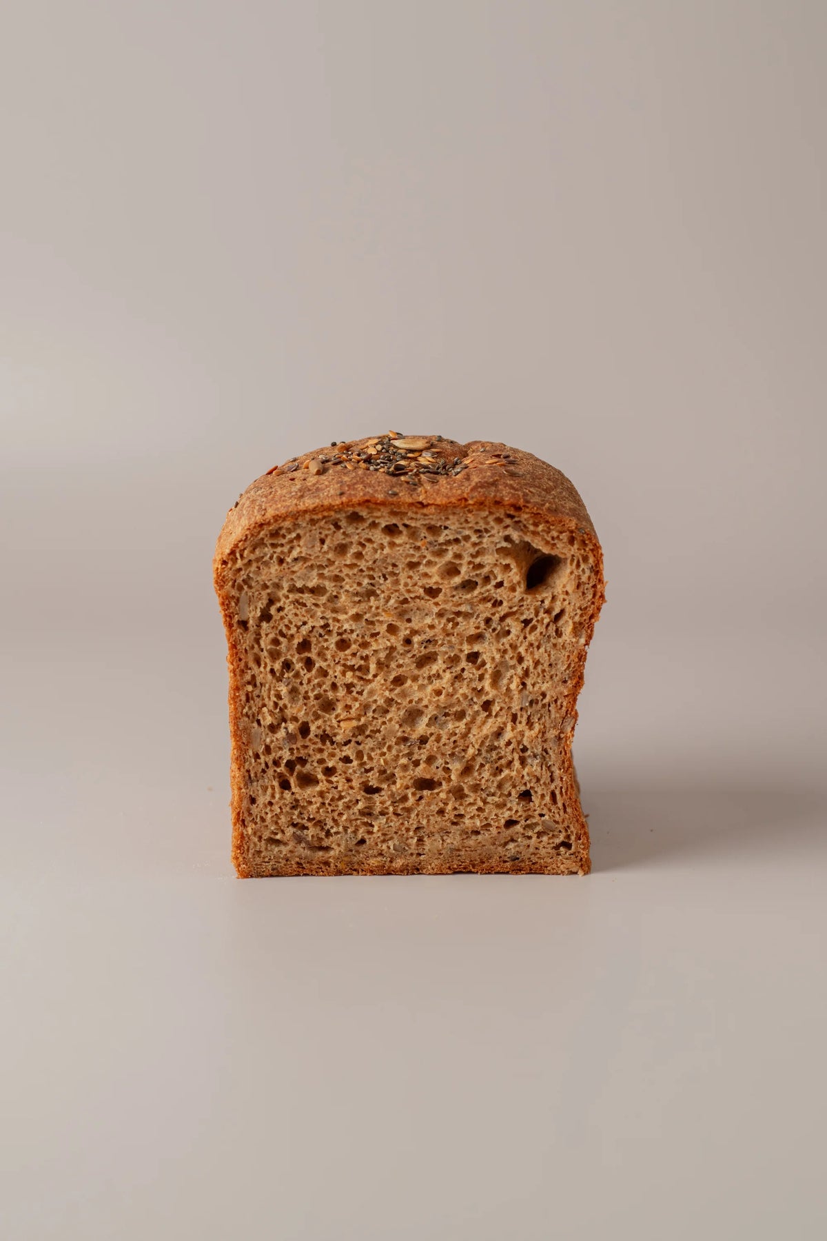 Rebanada de pan de molde con semillas sin gluten y sin lactosa mostrando su interior artesanal.
