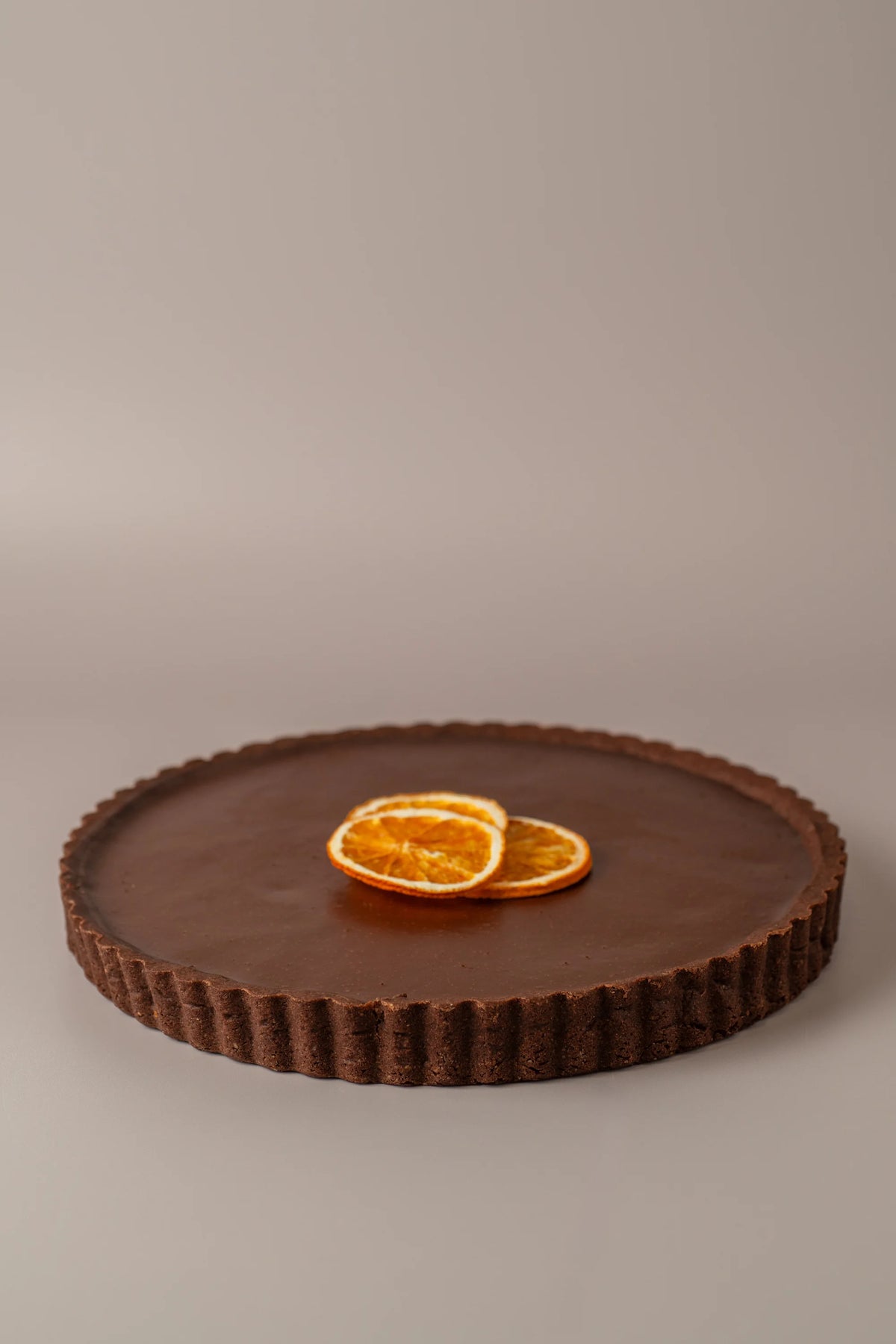 Tarta de chocolate y naranja sin gluten y sin lactosa de NICOLINA Madrid, con acabado brillante y decoración de naranja deshidratada.

