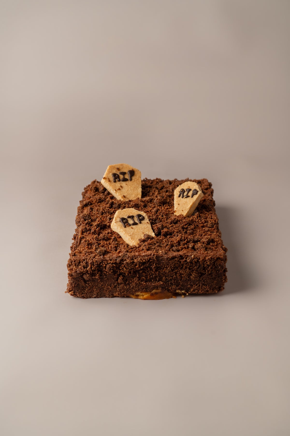 Detalle de Tarta de Halloween sin gluten y sin lactosa de NICOLINA Madrid, decorada con migas de chocolate y galleta en forma de lápida con texto RIP.